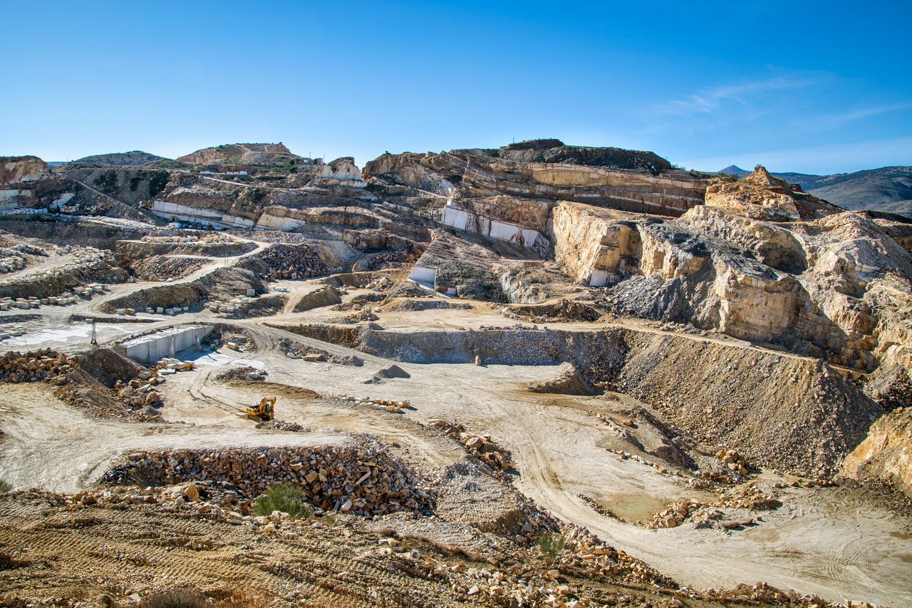 our-stories Wide view of a large open-pit quarry showing layers of rock and active heavy machinery.