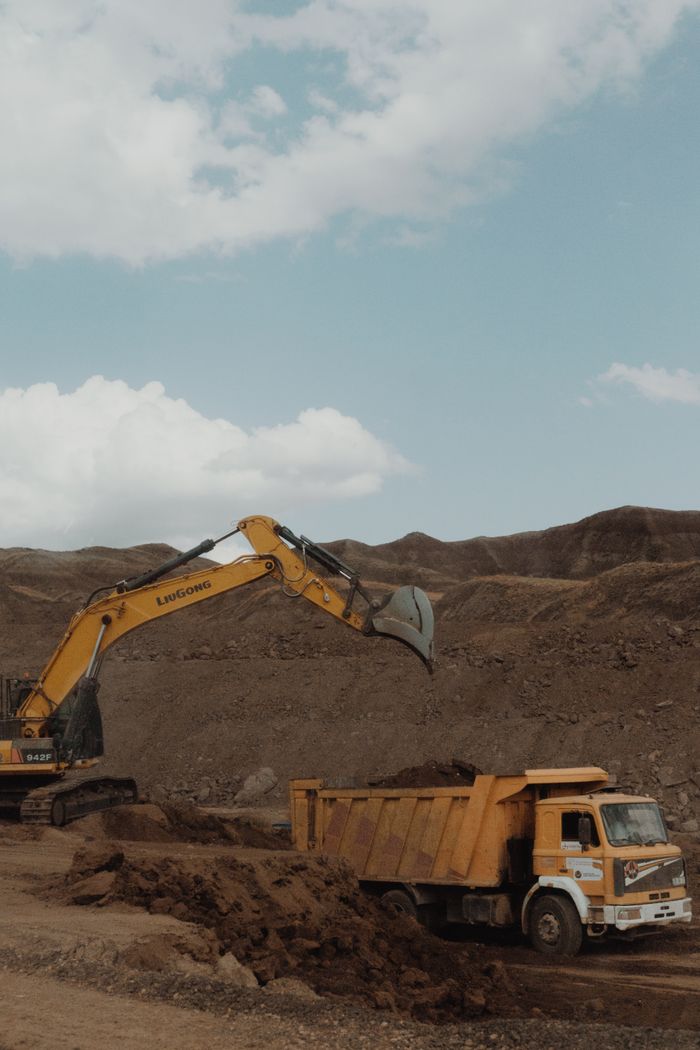 The Art of Drawing Readers In: Your attractive post title goes here Yellow excavator and dump truck operating in a mining setting under a blue sky.